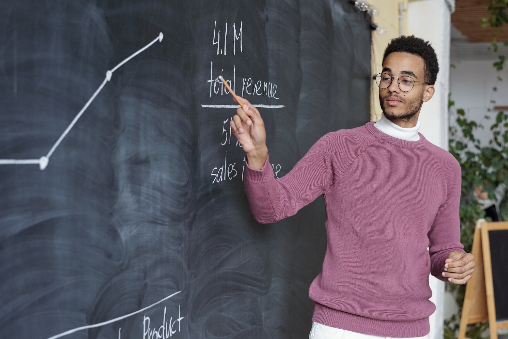 Young confident teacher of economics pointing at graph on blackboard